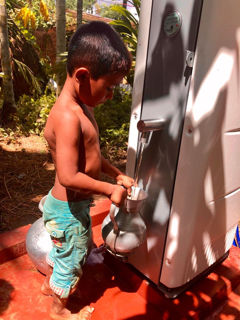 A boy filling a metal jug from the tap of a Villagepump 500 Electric