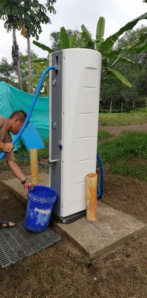 A man fills a blue bucket at a Villagepump installed on a concrete base in Colombia